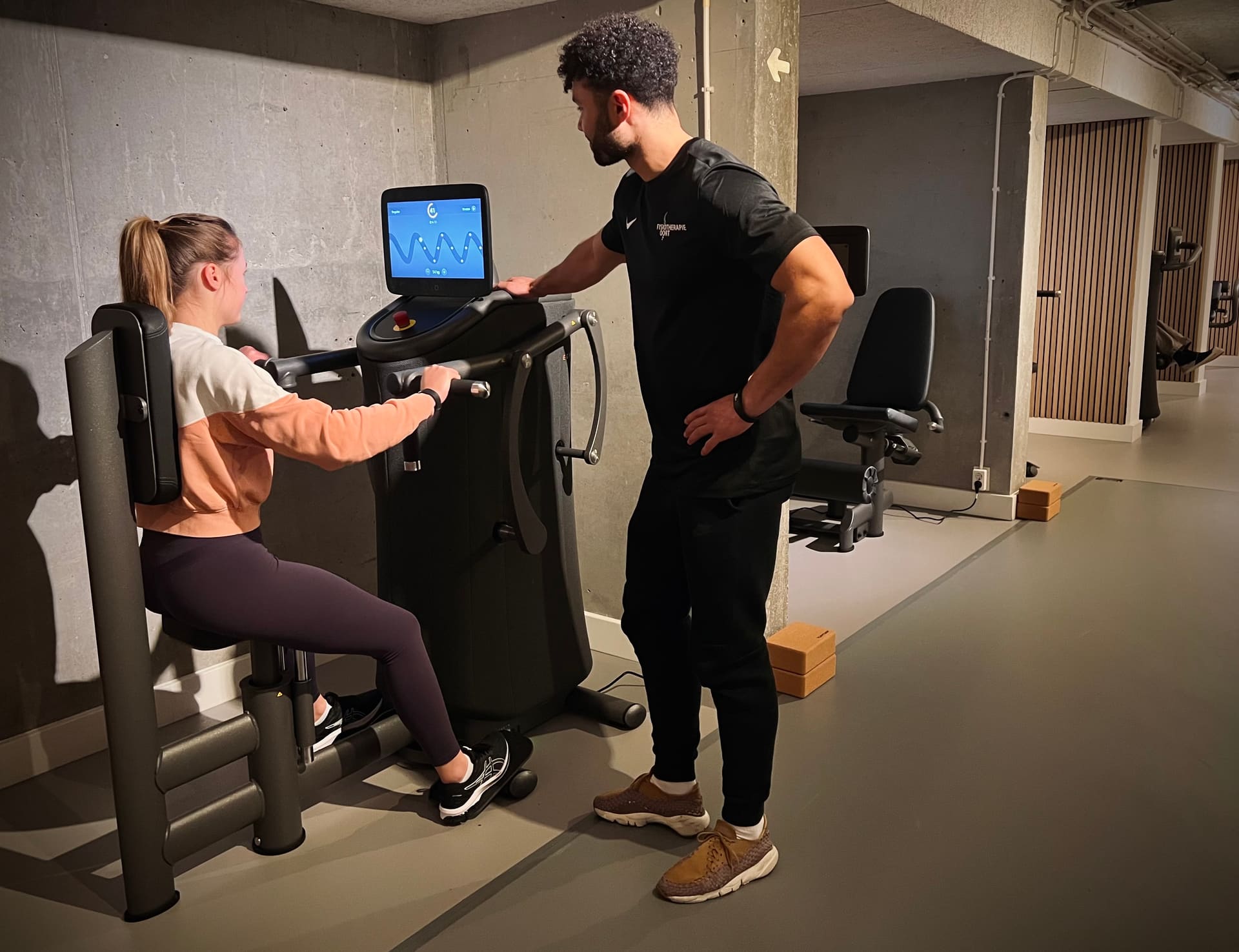 Een fitcoach van Fysiotherapie Oort begeleidt iemand op een EGYM krachttoestel